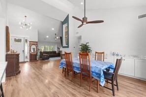 A spacious dining area with a high ceiling fan, wooden dining table, and chairs.