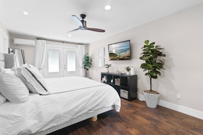 A bedroom with a bed, a ceiling fan, a TV, and a potted plant.