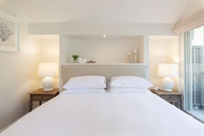 Een hotelkamer met een groot bed, twee nachtkastjes met lampen, een spiegel boven het bed en een raam met gordijnen.