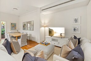 A modern living room with a dining area, a flat-screen TV, and artwork on the walls. - Waterfall Garden 3-Bed Home McMahons Point (McMahons Point)
