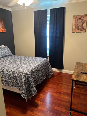 A bedroom with a bed, a wooden floor, a small table, and a window with curtains. - West Knox home w/Hot Tub and Fenced Backyard (Knoxville)