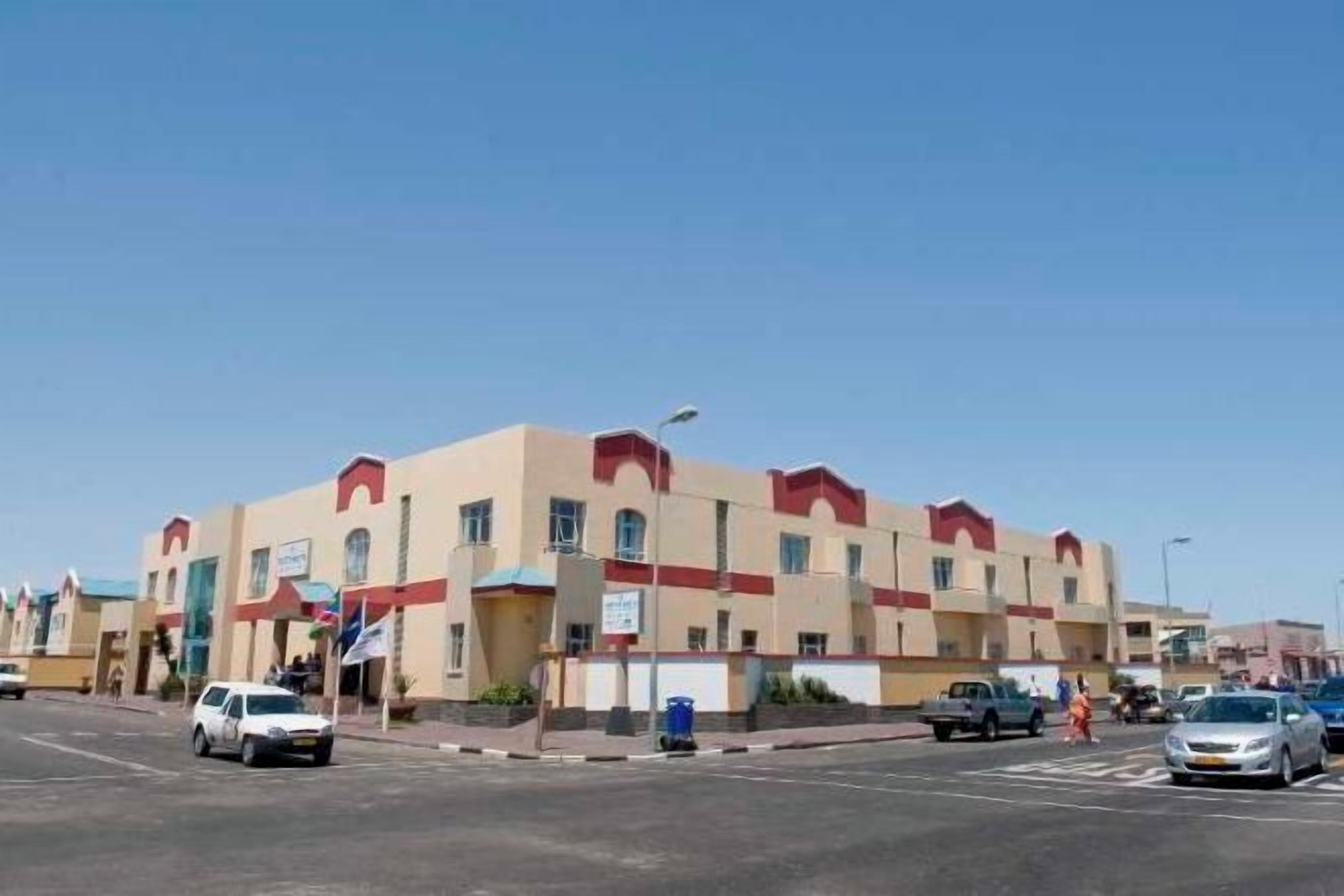 Un edificio de varios pisos con techo plano y un detalle rojo en la parte superior.