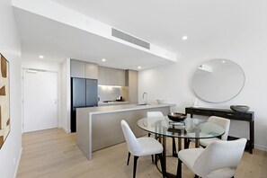 Eine moderne Küche mit einer zentralen Kochinsel, einem Essbereich mit einem Glastisch und weißen Stühlen sowie einem großen Spiegel an der Wand.