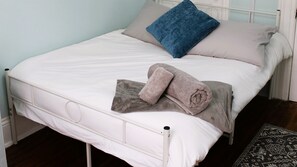 A bed with white bedding, a blue pillow, and two rolled towels. - Uptown Saint John Retreat (Saint John)