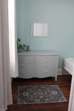 A bedroom with a white dresser, a small plant, and a patterned rug on a wooden floor. - Uptown Saint John Retreat (Saint John)