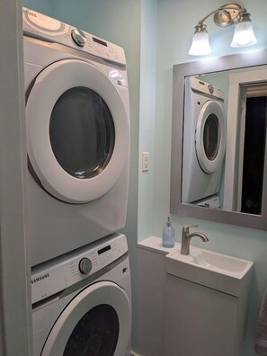 A laundry area with two stacked washing machines, a sink, and a mirror above the sink. - Uptown Saint John Retreat (Saint John)
