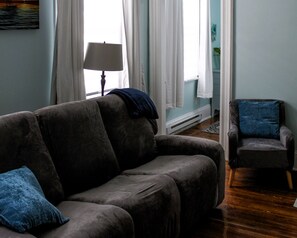 A living room with a sofa and armchair, a lamp, and a painting on the wall. - Uptown Saint John Retreat (Saint John)