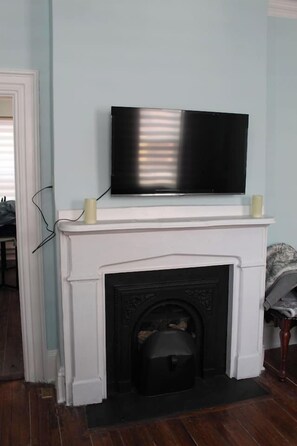 Habitación con chimenea blanca, un televisor de pantalla plana montado encima y una puerta que conduce a otra habitación.