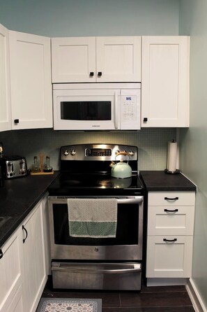 A kitchen with white cabinets, a microwave, a stove with a kettle, and a toaster. - Uptown Saint John Retreat (Saint John)