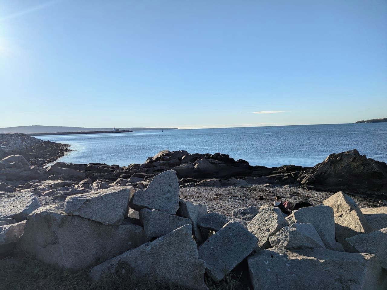 Un rivage rocheux, avec de gros blocs de pierre au premier plan et une mer calme à l’arrière-plan.
