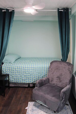Een kamer met een bed, een stoel, een plafondventilator en gordijnen.