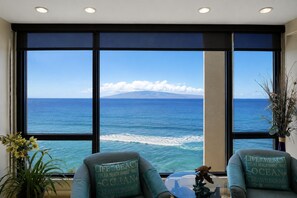 Habitación con amplias ventanas con vistas al océano, que incluye dos sillones con cojines de motivos marinos y una mesita con un adorno.
