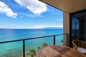 Un balcón con vista al océano, una mesa de madera y una silla.