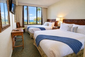 Ein Hotelzimmer mit zwei Betten, einem Schreibtisch, einem Sessel und Meerblick.