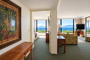 A hotel room with a large window, a television, a sofa, and a painting on the wall. - Oceanfront Ka'anapali Shores Corner Ground Floor Condo | Beach, Pools,  Sleeps 8 (Lahaina)