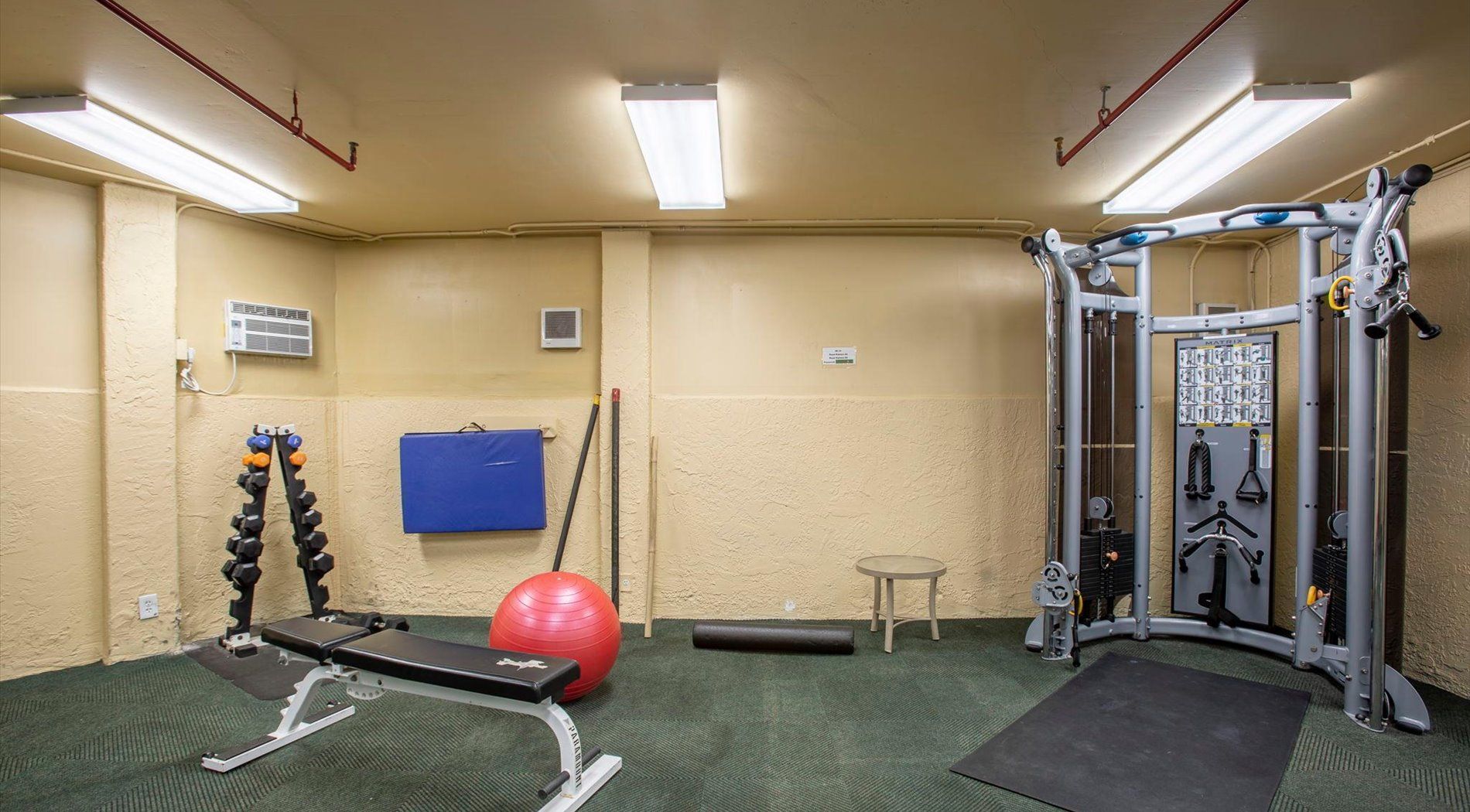 Une salle de sport équipée de matériel d’exercice, avec un ballon rouge et un tapis bleu.