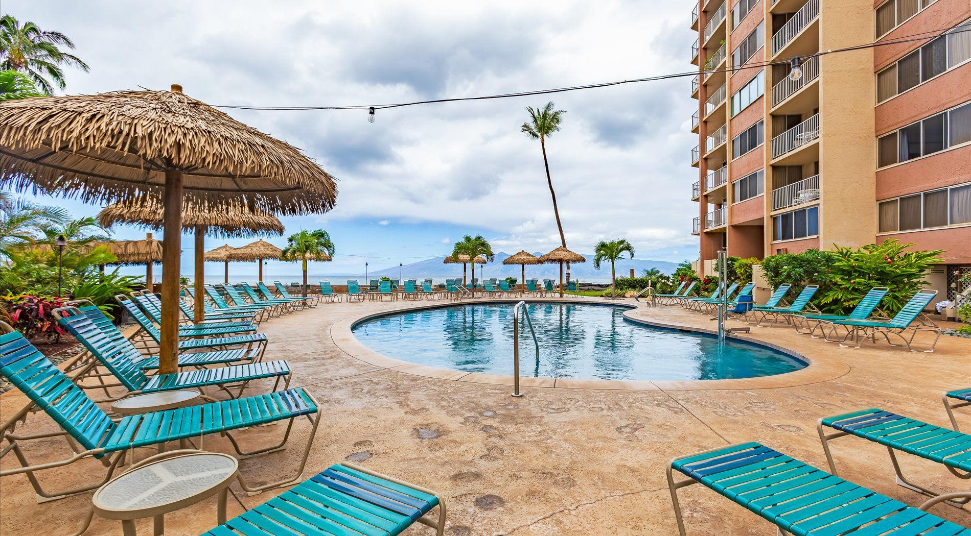 Ein Poolbereich eines Resorts mit Liegestühlen, einem Schwimmbecken und einem Gebäude mit Balkonen.