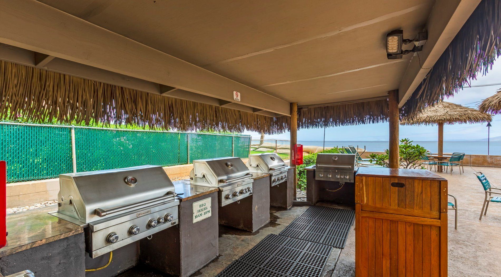 Un espace barbecue extérieur doté de plusieurs grils et d’un meuble en bois, avec vue sur une plage.