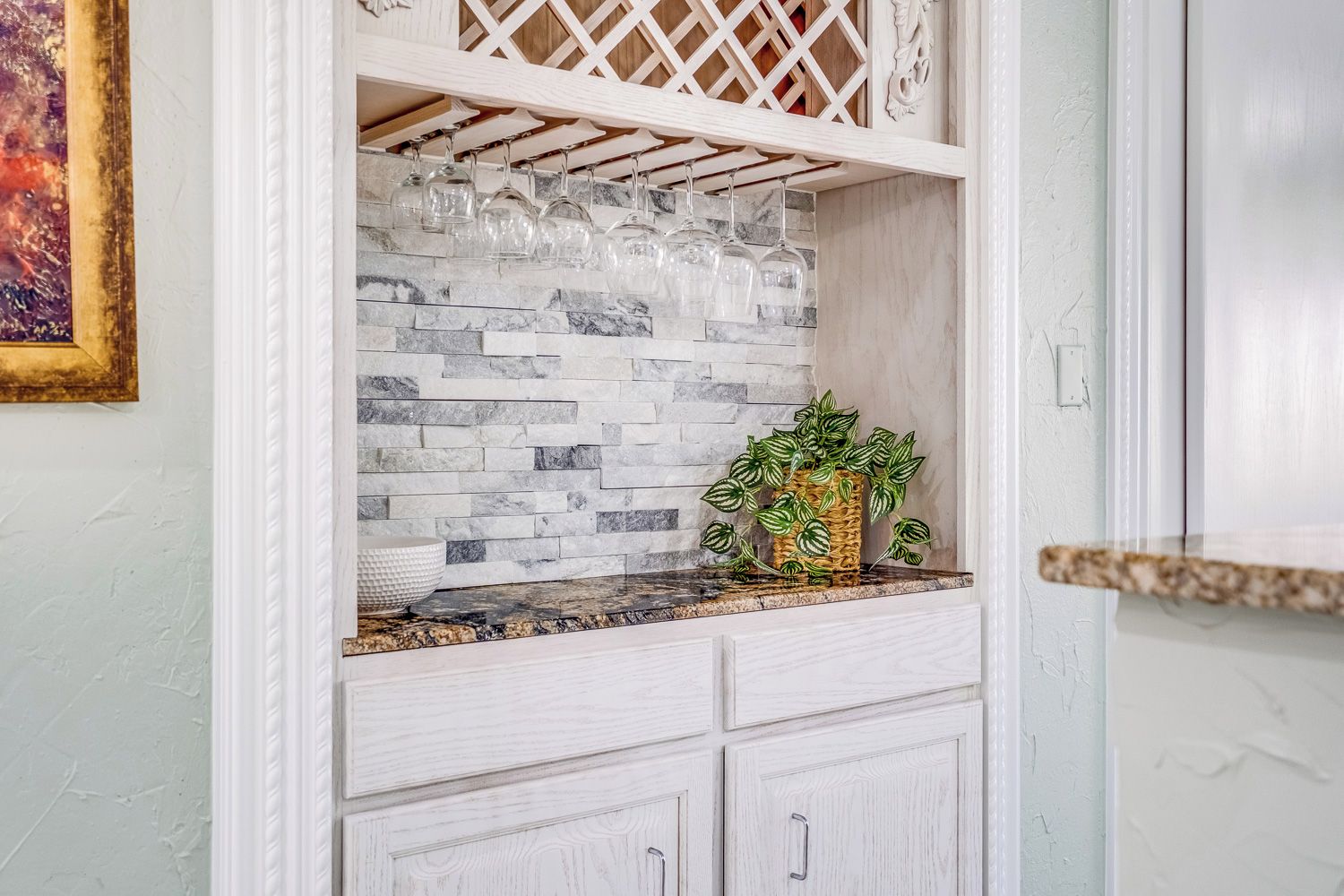 A kitchen with a marble backsplash, a plant on the counter, and a wine rack above.