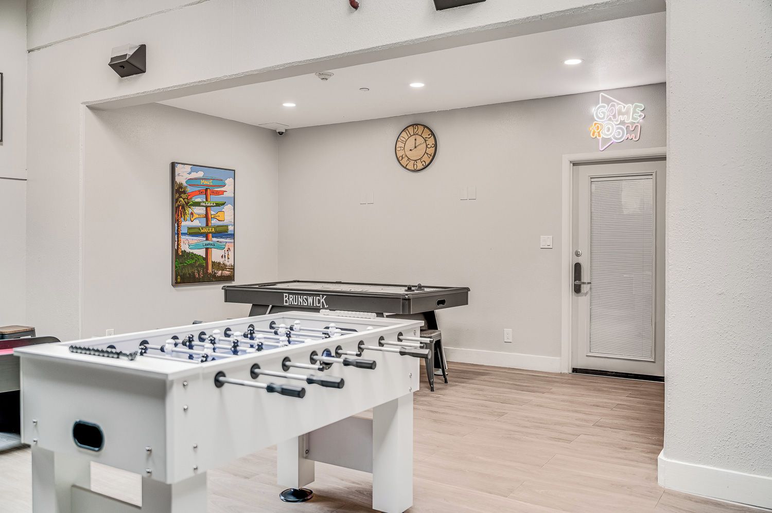 Een kamer met een tafelvoetbaltafel, een klok en een neonbord waarop staat 'GAME ROOM'.