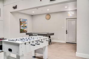 A room with a foosball table, a clock, and a neon sign reading 'GAME ROOM'. - Oceanfront Corner Penthouse | Pool, Hot Tub, Beach, Tennis, Pickleball, Dining (Lahaina)