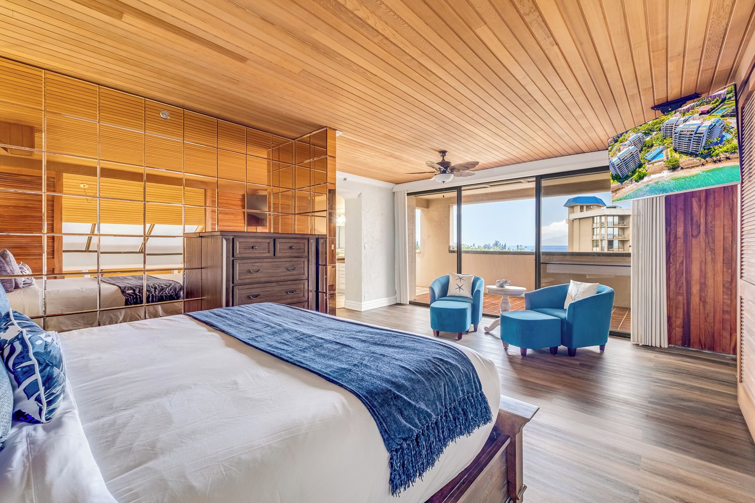 Une chambre moderne dotée d’un grand lit, d’une armoire, d’un coin salon avec deux fauteuils et d’un balcon offrant une vue sur les bâtiments et l’eau.
