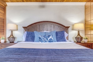 A bedroom with a large bed, wooden headboard, two bedside tables with lamps, and a blue textured bedspread. - Oceanfront Corner Penthouse | Pool, Hot Tub, Beach, Tennis, Pickleball, Dining (Lahaina)