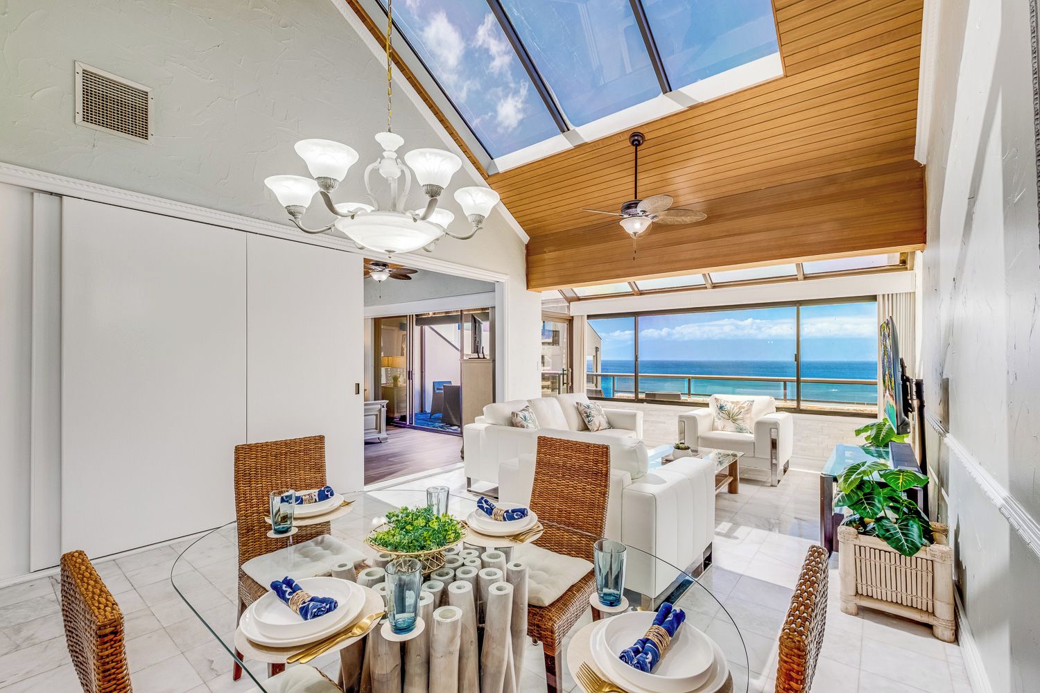 A spacious dining area with a glass table, white furniture, and a view of the ocean.