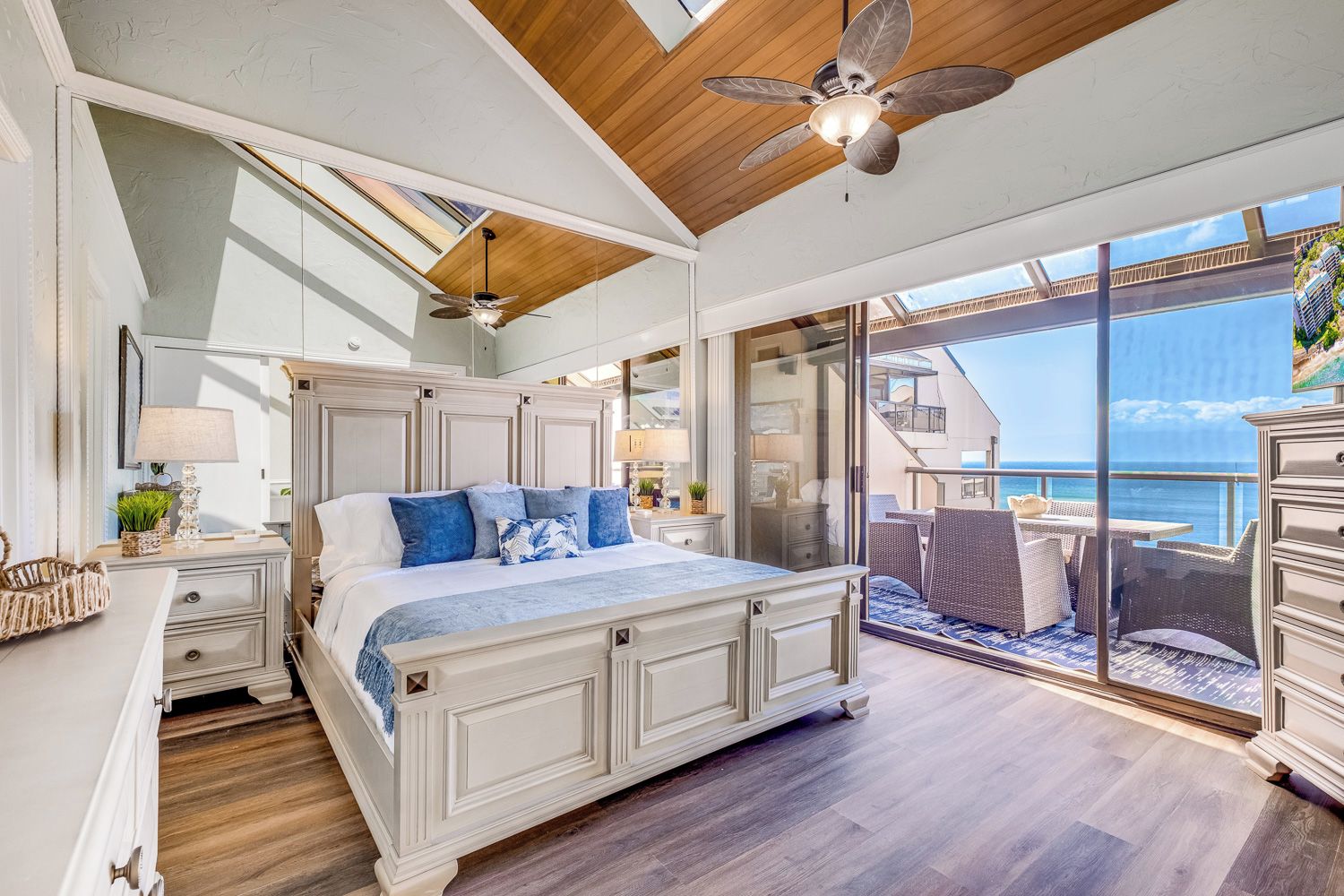 A bedroom with a large bed, a ceiling fan, and a view of the ocean.
