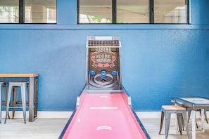 A shuffleboard table with a 'ROCKETS' sign, two metal stools, and a table with a 'HATRED GAMES' sign. - Oceanfront Corner Penthouse | Pool, Hot Tub, Beach, Tennis, Pickleball, Dining (Lahaina)
