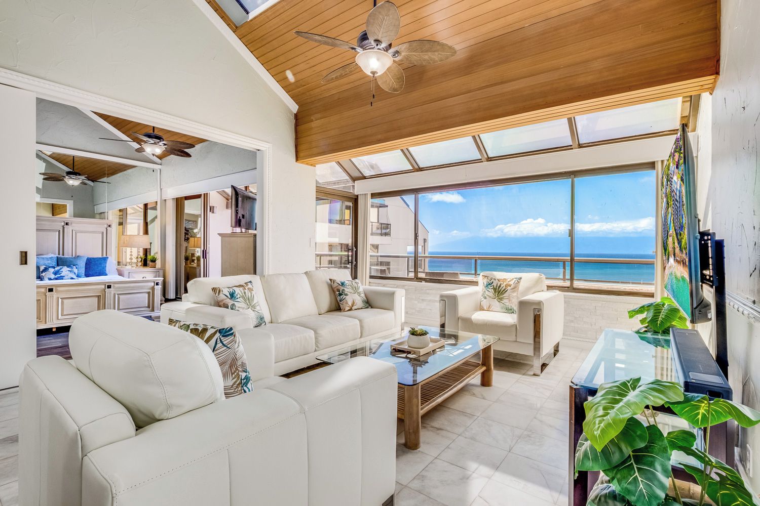 A spacious living area with a view of the ocean, a ceiling fan, and a dining area with a glass table.