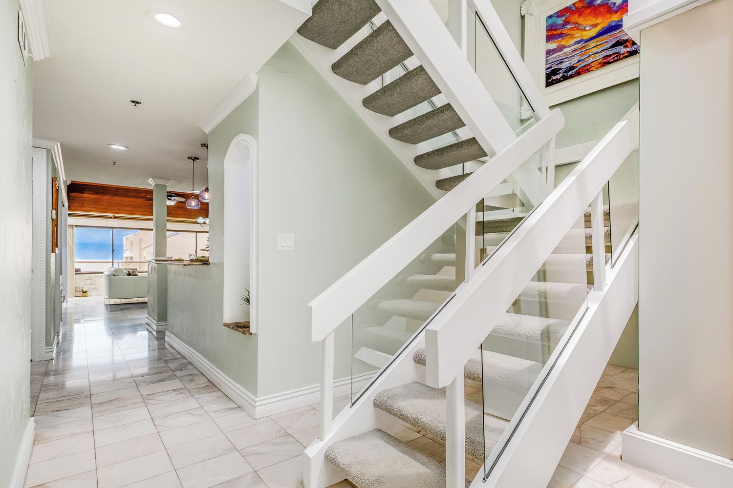 A modern interior with a staircase, a kitchen area, and a view to the outside.