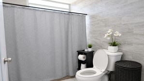 Een moderne badkamer met douchegordijn, toilet en een klein plankje met planten.
