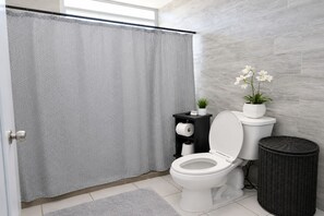 Ein modernes Badezimmer mit Duschvorhang, Toilette und einer kleinen Ablage mit Pflanzen.