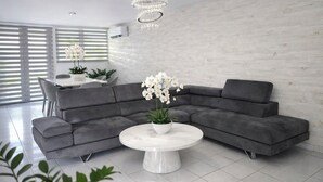 Een moderne woonkamer met een grijze modulaire bank, een ronde witte salontafel en een kroonluchter.