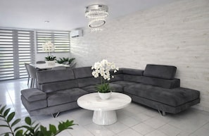 Ein modernes Wohnzimmer mit einem grauen Ecksofa, einem weißen runden Couchtisch und einem Kronleuchter.