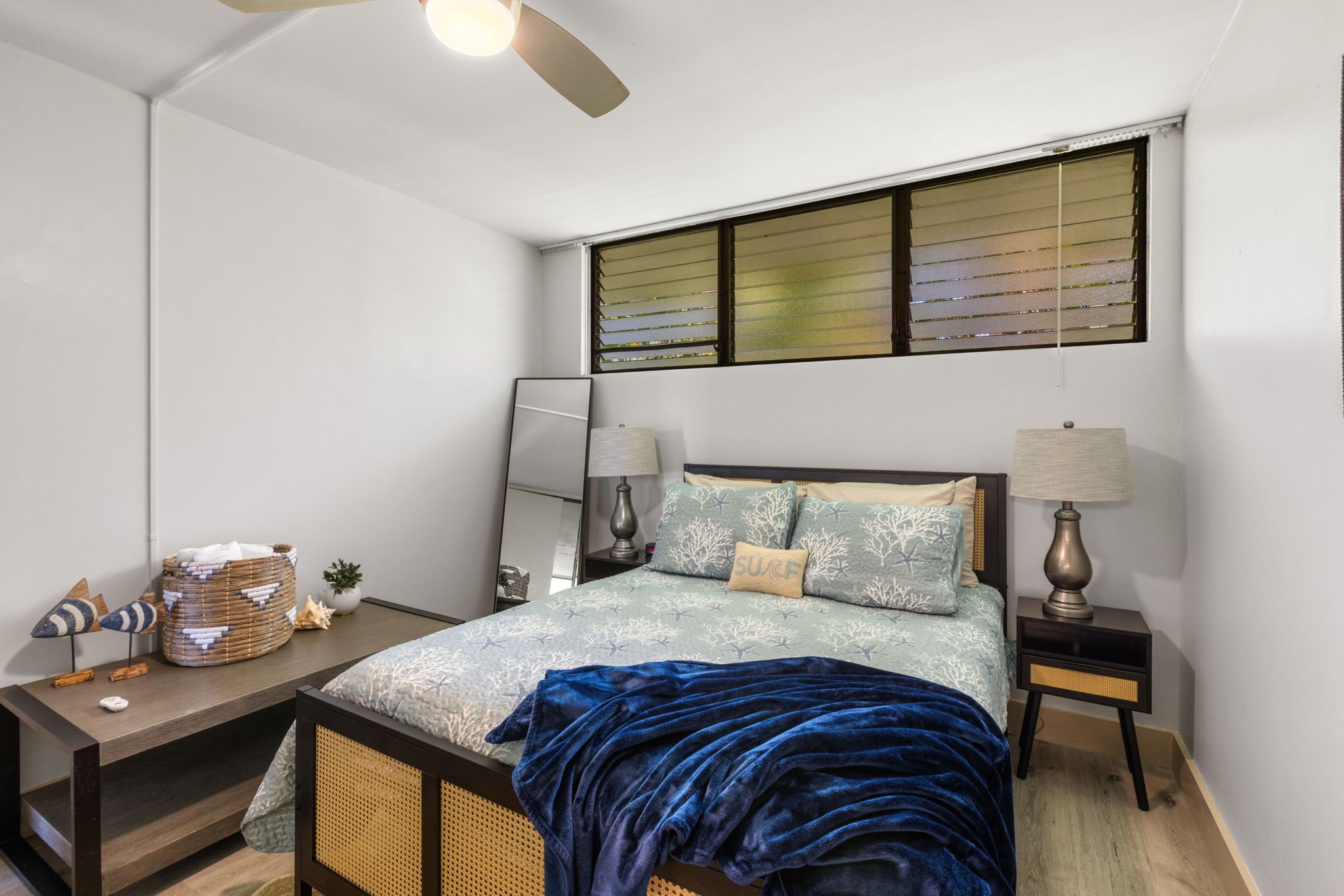 Ein Schlafzimmer mit einem Bett, zwei Nachttischen, einem kleinen Tisch, einem Deckenventilator und einem Fenster mit Jalousien.