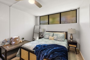 A bedroom with a bed, two bedside tables, a nightstand, a ceiling fan, and a window with blinds.
