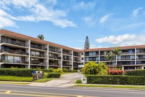 A multi-story hotel with balconies, a landscaped entrance, and a clear sky.