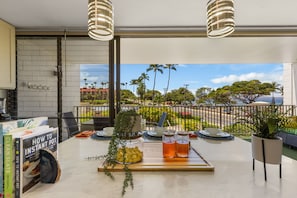A balcony with a table set for dining, a view of palm trees and a road, and a building in the background.