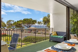 A balcony with a view of the street, a dining table set with plates and cutlery, a sofa with cushions, and a potted plant.