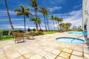 Área ao lado da piscina com hidromassagem, espreguiçadeiras e palmeiras.