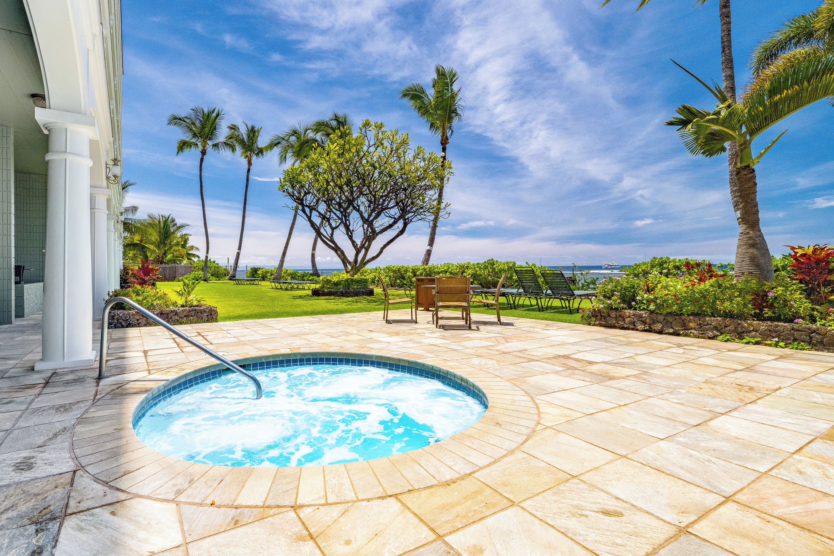 A pool area with a hot tub, outdoor seating, and a view of the ocean.