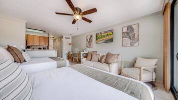 A hotel room with a bed, a sofa, a dining table with chairs, and a ceiling fan.