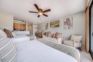 Quarto de hotel com cama, sofá, mesa de jantar e cadeiras, e um ventilador de teto.