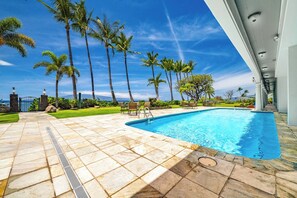 Zona de piscina con vista despejada al océano, rodeada de palmeras y un solárium con baldosas.
