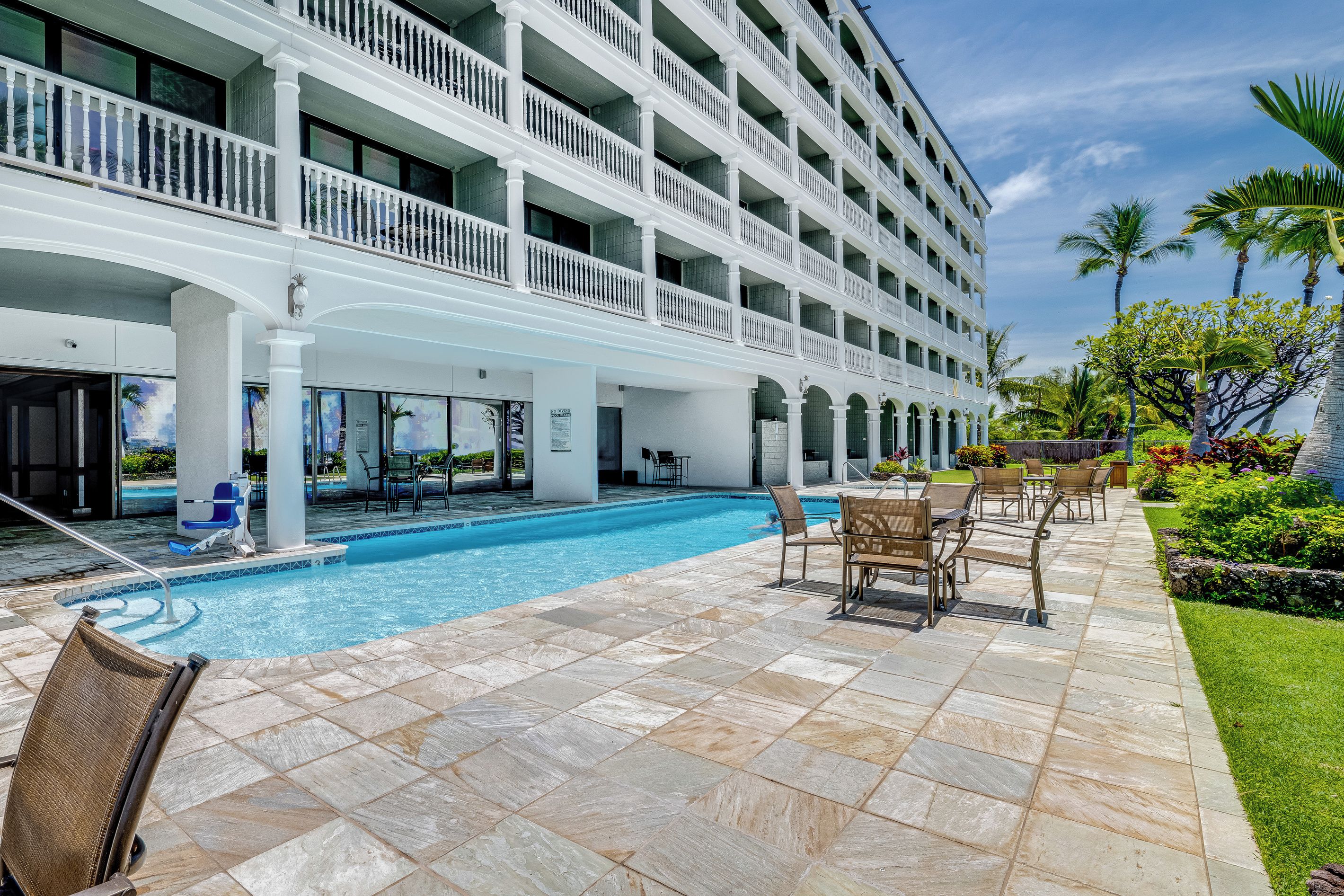 A hotel with a pool, outdoor seating, and a garden with palm trees.