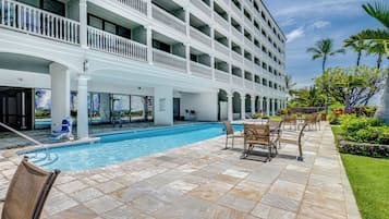 A hotel with a pool, outdoor seating, and a garden with palm trees.