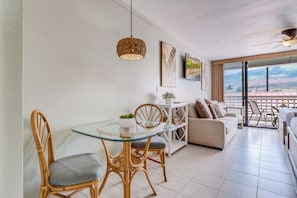 Una sala moderna con una mesa de vidrio, sillas de mimbre, un sofá y un balcón con vistas.