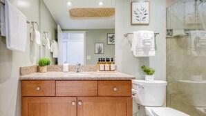 Een badkamer met een houten wastafelmeubel, een toilet, een douchegedeelte en diverse toiletartikelen op het aanrecht.
